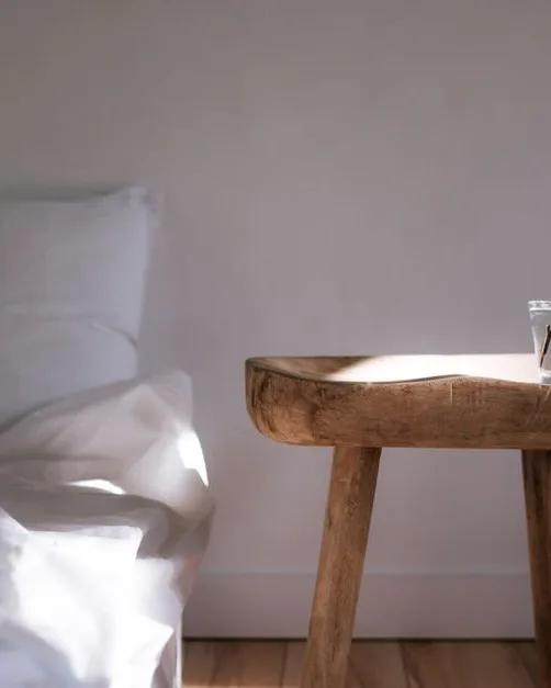 Chambre baignée de lumière au réveil, linge de lit blanc et table de chevet en bois avec une plante